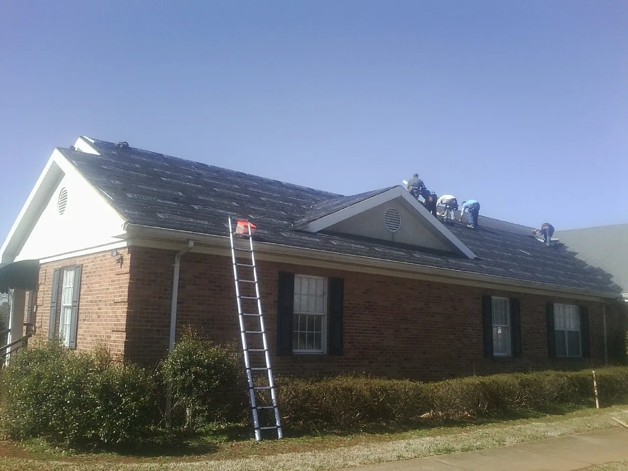 Crew tearing shingles off a brick ranch roof with a ladder set — Metal Roof Repair work by our crew in Felt