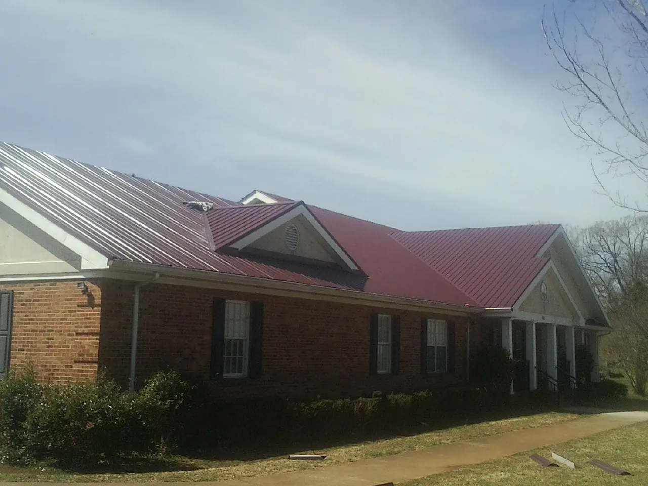 Red metal roof with gabled entries on a long brick building, from a Hail Damage Roof Repair job in Felt