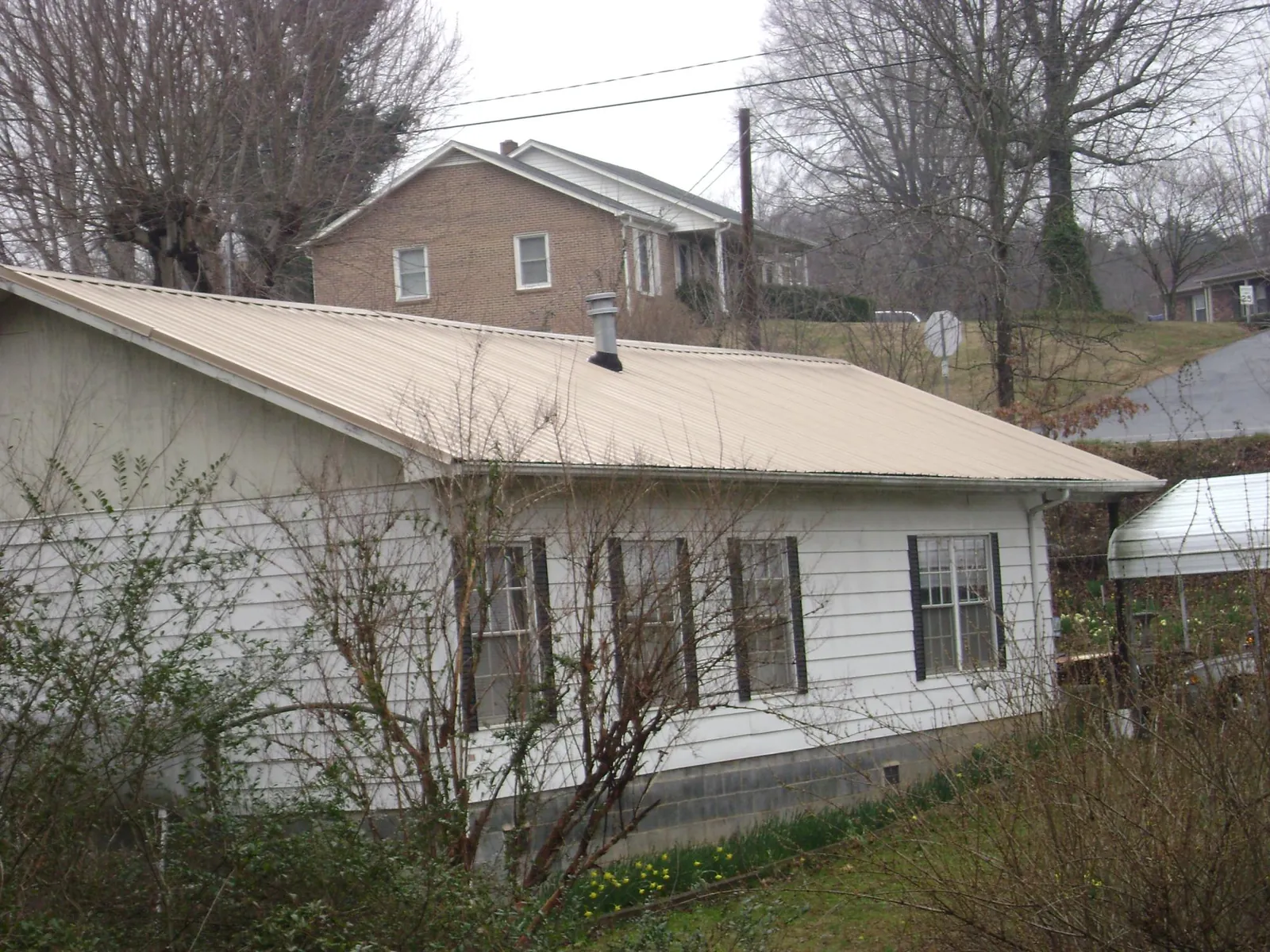 Tan metal roof on a white sided house set into a hillside — Commercial Roofing by Roofing Brothers in Felt