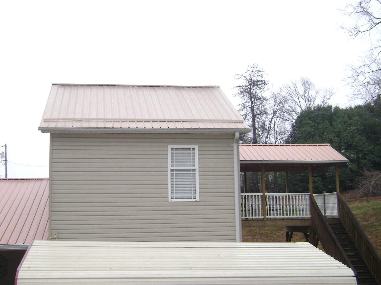 Tan metal roofs on a two story addition and attached porch, from a Roof Replacement job in Felt